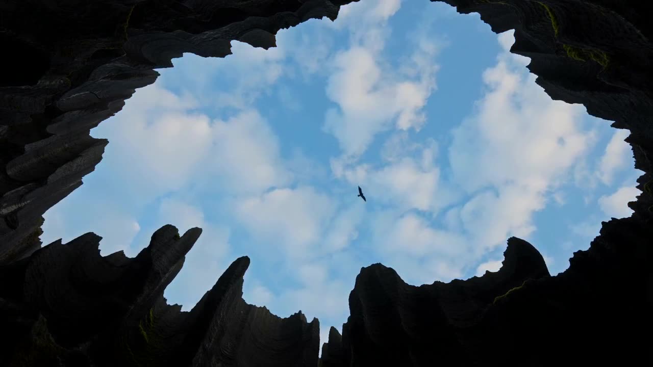 Looking up through a rock opening at a bright sky, a single bird in flight